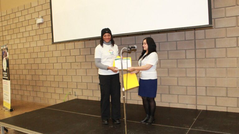 A certificate being handed to a participant on stage beneath a ToLSO banner.