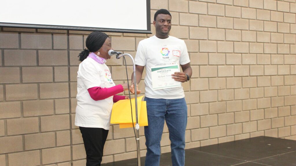 A young man in an "I AM ToLSO" shirt receiving a participation certificate.
