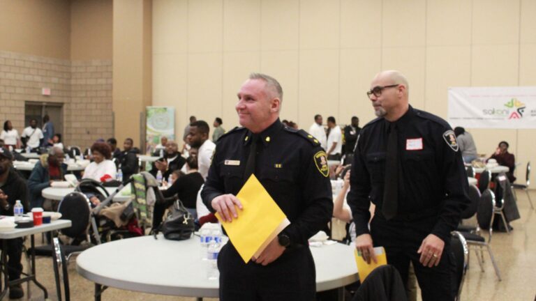 Two Windsor Police officers carrying certificate envelopes through a dining hall.