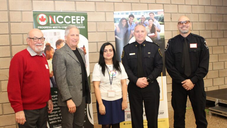 Five people, including police officers and an organizer in a ToLSO shirt, posing between NCCEEP and youth banners.
