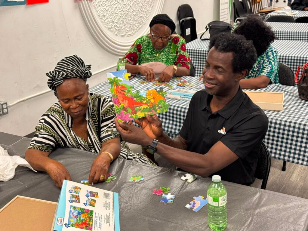 Two members holding up a finished jigsaw of a landscape, both smiling