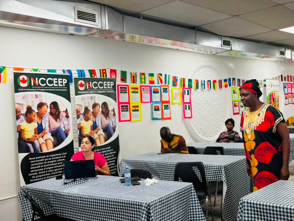 The Kitchener meeting room with NCCEEP banners and a row of flags along the wall, a woman standing at the side