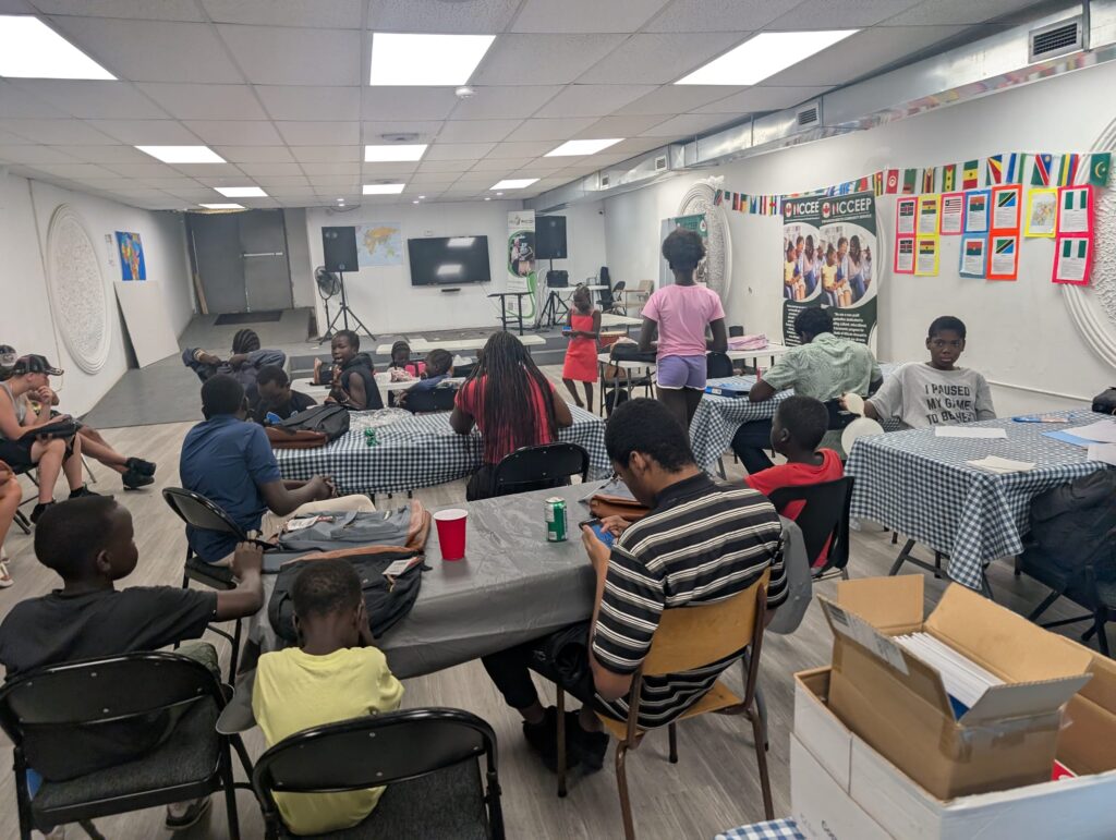 Families seated at tables in the hall at the Windsor centre on Tecumseh Road, backpacks and boxes of supplies around them