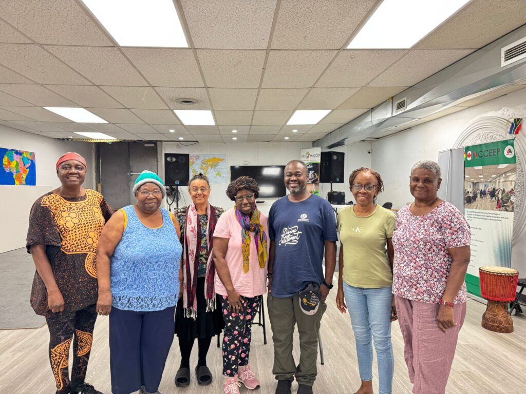 Seven attendees standing together in a line at the front of the hall at the Windsor centre on Tecumseh Road, a hand drum on the floor beside them and a Seniors Active Living Centre banner to the right