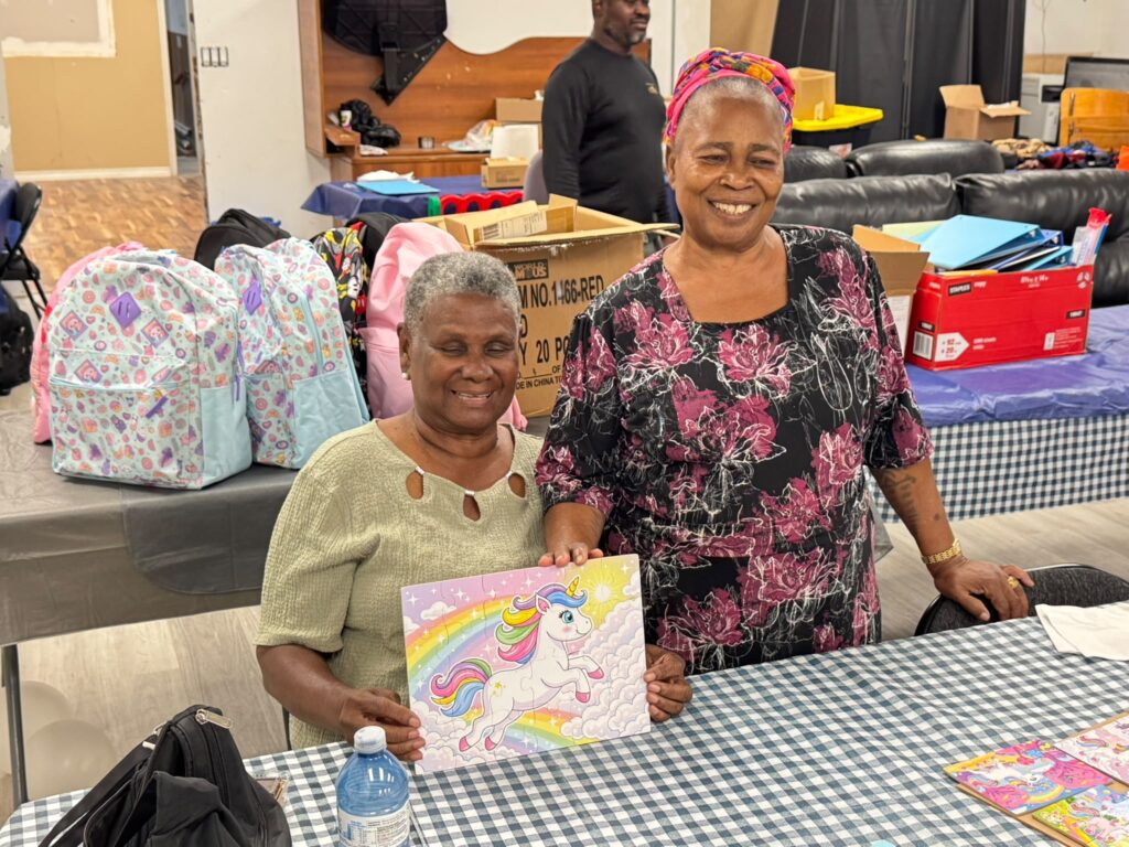 Two attendees holding up the pictures they have coloured in, a rainbow and unicorn design, smiling at the camera